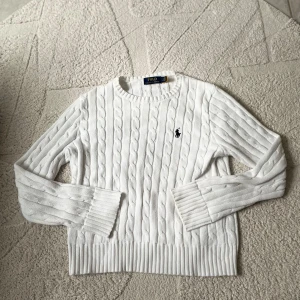 Vit tröja från Polo Ralph Lauren - Säljer en stilren vit kabel tröja från Polo Ralph Lauren med det klassiska logotypbroderiet på bröstet. Tröjan har en kabelstickad design och långa ärmar, perfekt för kyligare dagar. I storlek S men kan nog passa xs 