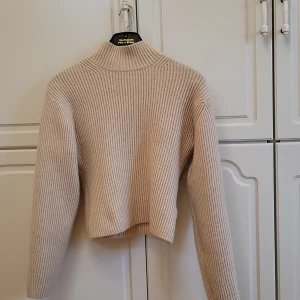 Beige stickad polotröja - Säljer en stilren beige stickad polotröja med ribbad design. Tröjan har långa ärmar och en croppad passform.