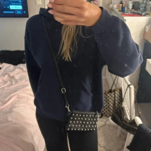 Svart axelväska med nitar - Säljer en ball svart axelväska med silverfärgade nitar. Väskan har en justerbar axelrem och en dragkedja på baksidan för extra säkerhet. Perfekt för en utekväll eller när du vill lägga till lite edge till din outfit!