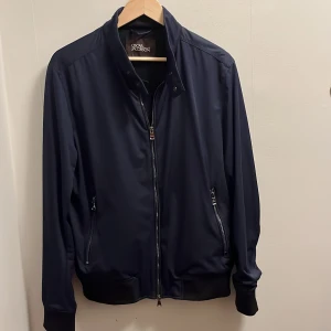 Oscar Jacobson jacka - Harringtonjacka från Oscar Jacobson. Jackan är tillverkad i en lätt och mjuk polyesterväv, och blir en riktig stilhöjare under vår- och höstdagar då den går fint ihop med en dressad stil.