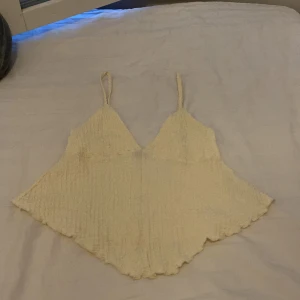 Beige topp från Gina Tricot - Säljer en superfin beige topp från Gina Tricot. Den är ärmlös med smala axelband och har en härlig, lite krinklad textur. Perfekt för sommaren och kan lätt matchas med både jeans och kjol. Toppen är i storlek M och är i nyskick.