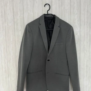 Jack & Jones grå kavaj - En grå kavaj med två knappar framtill. Kavajen har en ficka på bröstet och två fickor på sidorna. Kavajen har även en innerficka. Kavajen är i gott skick.