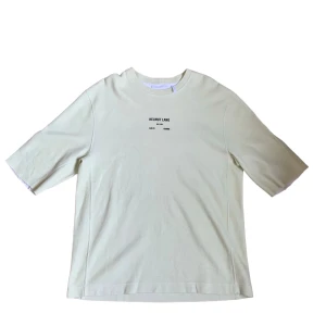 Beige t-shirt från Helmut Lang - Säljer en stilren beige t-shirt från Helmut Lang med tryck på bröstet. T-shirten har en normal passform och är kortärmad, perfekt för vår och sommar. Materialet känns mjukt och skönt mot huden.