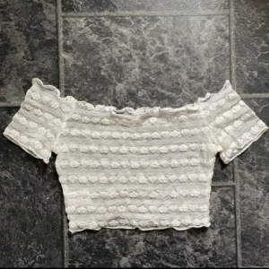 Vit offshoulder topp - Säljer en superfin vit offshoulder topp med korta ärmar. Toppen är croppad och har ett snyggt spetsmönster som ger en romantisk känsla. Perfekt för sommarens fester eller en dag på stan! Jag har på mig nippel covers under, därav syns dem igenom. Den är menad att vara som en topp man har över en bikini men man avgör själv hur man vill använda den. Passar både XS/S. Om man är storlek S blir det en lite tajtare passform.