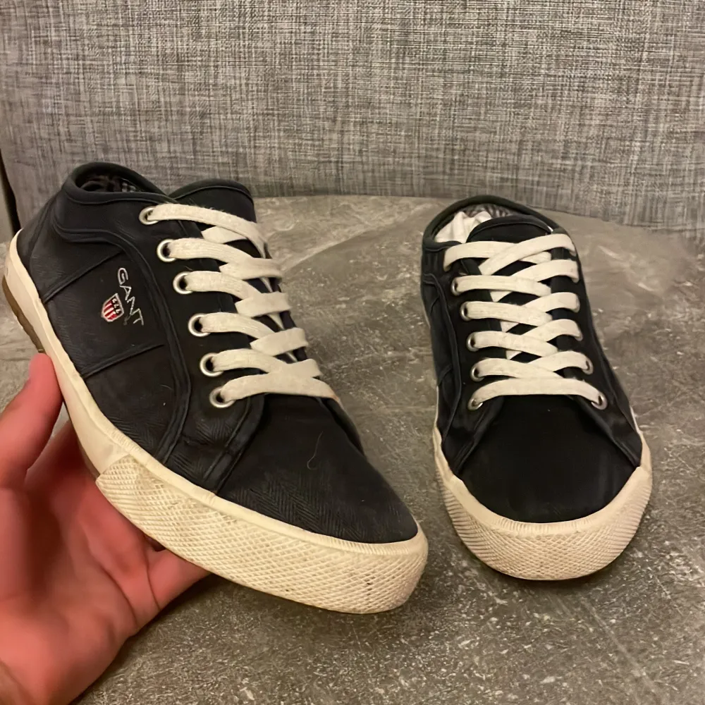 Säljer ett par snygga svarta sneakers från GANT. De har en klassisk design med vita snören och en vit sula. Skorna är i bra skick och har GANT-loggan broderad på sidan. Perfekta för vardagsbruk!. Skor.