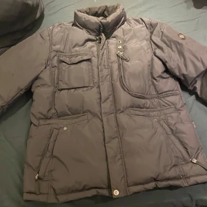 Svart vinterjacka från Hollies - Säljer en svart vinterjacka från Hollies med flera praktiska fickor och dragkedja. Jackan har en hög krage och knappar för extra skydd mot kylan. Perfekt för kalla dagar!