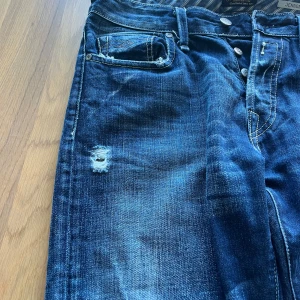 Blå jeans från Replay - Snygga blå jeans från Replay med slitna detaljer och knappgylf. Klassisk femficksdesign och broderade bakfickor. Perfekta för en avslappnad stil. Priset kan diskuteras.