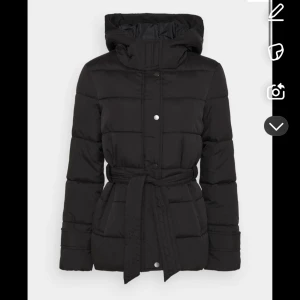 Svart dunjacka med bälte - Snygg svart dunjacka med bälte i midjan och dragkedja framtill. Jackan har långa ärmar och en hög krage för extra värme. Perfekt för kyliga dagar. Använts 2 gånger och säljs nu då jag fick två liknande i julklapp 