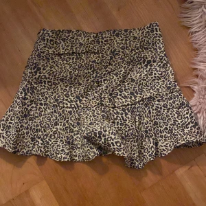 Leopardmönstrad kjol från Zara - Snygg leopardmönstrad kjol från Zara i en kort modell. Kjolen har volangdetaljer och en omlott-design som ger en trendig look. Perfekt för att sticka ut med stil! 🐆🐆