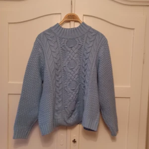 Ljusblå stickad tröja - Säljer en mysig ljusblå stickad tröja med flätmönster. Tröjan har en halv krage och långa ärmar, perfekt för kyliga dagar. Den är i storlek XS och passar utmärkt för höst och vinter. Jag är en S/M så det funkat med