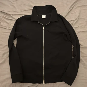 Svart jacka från Selected Homme - Snygg svart jacka från Selected Homme med dragkedja framtill. Jackan har en klassisk krage och långa ärmar, perfekt för en stilren look. Tillverkad i ett mjukt material för extra komfort.