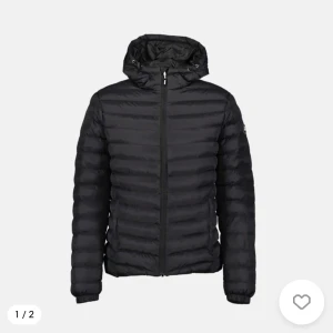 Svart dunjacka med huva - Säljer en svart dunjacka med huva och dragkedja. Jackan har en quiltad design och långa ärmar, perfekt för kyligare väder. Den är stilren och enkel att matcha med olika outfits.