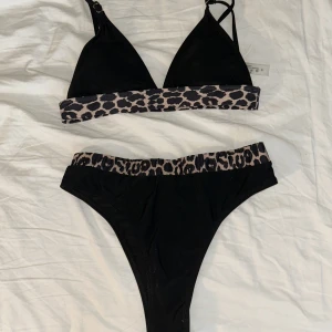 Svart bikini med leoparddetaljer - Trendig svart bikini med leopardmönstrade detaljer. Överdelen har smala axelband och en bred leopardkant under bysten. Underdelen är högmidjad med matchande leopardkant. Säljer då överdelen är för liten.