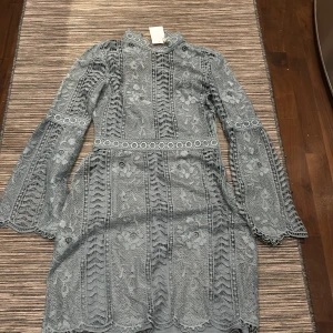 Blå spetsklänning från H&M - Elegant blå spetsklänning från H&M med vackra blommiga detaljer. Klänningen har långa ärmar och en figursydd passform som framhäver midjan. Perfekt för speciella tillfällen.