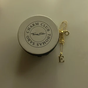 Guldhalsband med bokstav från Thomas Sabo - Elegant guldhalsband från Thomas Sabo med en charm i form av bokstaven 'E'. Perfekt för att ge en personlig touch till din stil. Halsbandet kommer i en snygg förpackning från Charm Club.💕💕 Ny pris 999kr(Aldrig använt)