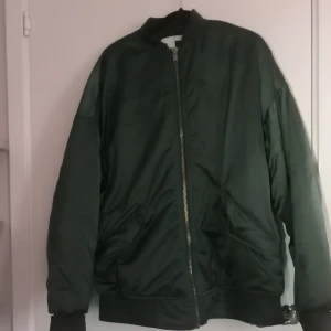 Grön bomberjacka från H&M - Säljer en stilren grön bomberjacka från H&M. Jackan har en dragkedja framtill och långa ärmar. Perfekt för en cool och avslappnad look.