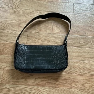 Svart axelväska från Gina Tricot - Snygg svart axelväska från Gina Tricot. Väskan har en praktisk dragkedja upptill och en justerbar axelrem. Perfekt för att ge din outfit en trendig touch.