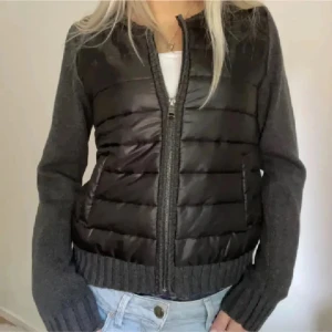 Svart och grå jacka med dragkedja  - Snygg svart och grå pufferjacka med dragkedja framtill. Jackan har långa ärmar och en quiltad design på framsidan. Perfekt för kyligare dagar. ( liten defekt inne i jackan som man inte tänker på skriv för bild )