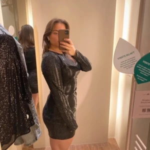 Svart glittrig klänning - Snygg svart glittrig klänning med långärmad design. Perfekt för en kväll ute med vänner. Klänningen har en tight passform som framhäver figuren.