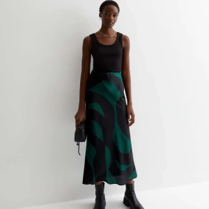 Svart och grön långkjol - Säljer en superfin svart och grön långkjol med ett coolt abstrakt mönster. Kjolen är perfekt för både vardag och fest och har en skön passform. Materialet känns lyxigt och faller snyggt. Passar perfekt med en enkel topp och boots!