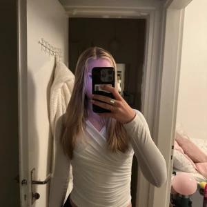 Vit omlottopp från Gina Tricot - Säljer en superfin vit omlottopp från H&M. Den är långärmad och har en snygg omlottdesign som ger en stilren look. Perfekt för både vardag och fest! Toppen är i mycket bra skick och passar till det mesta i garderoben.