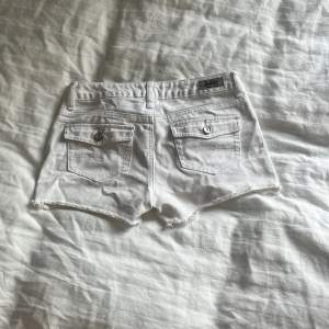 Säljer ett par snygga vita jeansshorts från justice. De har en klassisk femficksdesign med coola silverfärgade knappar. Shortsen är i en fräsch vit färg och har en rå kant nertill för en avslappnad look. Perfekta för sommardagar eller festivaler!