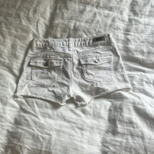 Vita jeansshorts från Lee - Säljer ett par snygga vita jeansshorts från justice. De har en klassisk femficksdesign med coola silverfärgade knappar. Shortsen är i en fräsch vit färg och har en rå kant nertill för en avslappnad look. Perfekta för sommardagar eller festivaler!