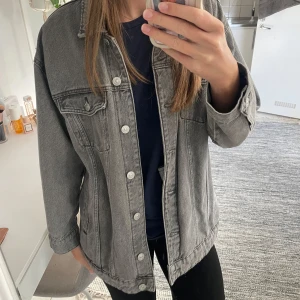 Grå jeansjacka - Säljer en snygg grå jeansjacka i oversized stil. Den har långa ärmar och knappar framtill. Perfekt för en avslappnad look och passar till de flesta outfits. Jackan är i bra skick och redo för en ny ägare!