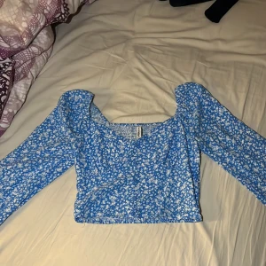 Somrig blå långärmad blus/topp - Jag säljer en jätte fin blå somrig tröja med vita blommor på. använd ett fåtal gånger och finns inte längre att köpa i butik. Jätte fin form på toppen då de finns en uringning med knappare. Pris kan diskuteras🥰 