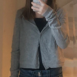 Grå kofta - Säljer en stilren grå kofta med långa ärmar. Perfekt för lager-på-lager och passar till många olika outfits. Koftan har en enkel design med knappar framtill.