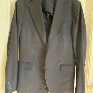 Till salu: Oscar Jacobson-kavaj i Drago 160’s-tyg - Säljer en elegant kostymkavaj från Oscar Jacobson, tillverkad i exklusivt Drago 160’s-tyg (producerat i Italien) från Luxury Collection.  Detaljer: ✔️ Färg: Svart ✔️ Storlek: M ✔️ Material: Högkvalitativ ull ✔️ Klassisk och stilren passform  Skick: Kavajen är i gott skick, men har en reva på vänster ärm (se bild).