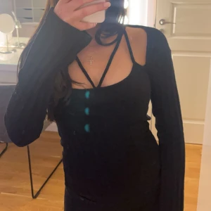 Svart ribbad topp från nelly - Snygg svart ribbad topp med långa ärmar och unika axelband. Perfekt för en stilren look. Toppen har en tight passform och är tillverkad i ett mjukt material. Aldrig använd