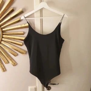 Svart body med tunna axelband - Elegant svart baddräkt med tunna axelband och enkel design. Perfekt för en stilren look vid poolen eller stranden.