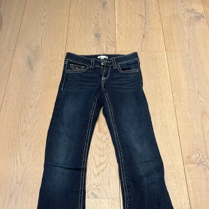 Mörkblå jeans från Gina Tricot - Snygga mörkblå jeans från Gina Tricot med kontrastsömmar och klassisk femficksdesign. Jeansen har en bootcut-stil och är perfekta för en avslappnad look. De är tillverkade i ett slitstarkt denimtyg och har en knapp- och dragkedjestängning framtill.