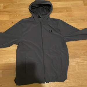 Grå jacka  från Under Armour - Säljer en grå jacka från Under Armour. Köpte den för 800 på stadium, är i helt ny skick och är ej använd. Kom privat för mer bilder kvitto osv. (Storlek M,men passar L också) pris går att diskuteras vid snabb affär