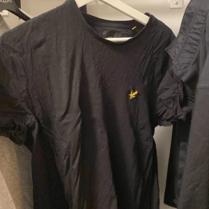 T shirt lyle & scott - Snygg svart t-shirt från Lyle & Scott med en liten broderad logga på bröstet. Perfekt för en stilren look. Kortärmad och i mjukt material för bekväm passform.