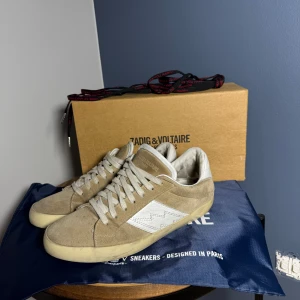  Zadig & Voltaire sneakers  - Snygga beige sneakers i mocka från Zadig & Voltaire med vita detaljer. Perfekta för en stilren look och perfekta nu till våren. Skorna har en klassisk design med en bekväm passform. Priset är inte hugget i sten. Kontakta mig vid fler frågor!!
