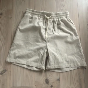Beige manchester shorts med snörning - Snygga beige shorts i manchester med elastisk midja och snörning. Perfekta för en avslappnad stil. De har en bakficka för extra funktionalitet.