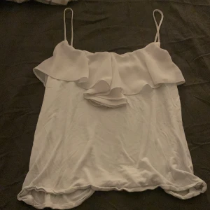 Vit linnetopp med volangdetalj - Säljer en söt vit linnetopp med smala axelband och volangdetalj framtill. Perfekt för varma sommardagar eller som ett lager under en kavaj. Toppen har en luftig och bekväm passform. Det står att det är L men passar som M/S💗 Använd 5-6 gånger inga fläckar 