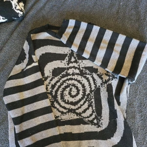 Svart och grå randig tröja med stjärnmönster - ALL PÄLS ROLLAS BORT VID FÖRSÄLJNING,  var lat och tog inte bort allt för bilden... Säljer en unik svart och grå tröja med ett coolt stjärnmönster i mitten. Tröjan har långa ärmar och ett randigt mönster som ger en modern look. Perfekt för dig som vill sticka ut!