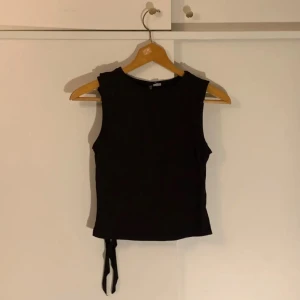 Svart ärmlös topp - Snygg svart ärmlös topp med knytning i sidan. Perfekt för en stilren look och kan enkelt matchas med olika outfits.