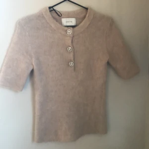 Beige tröja från H&M Edition - Säljer en stilren beige tröja från H&M Edition med tre glittriga knappar framtill. Tröjan har korta ärmar . Perfekt för en lite festligare look . Köpt nyss, användt 2/3 gånger, kommer tyvärr inte till användning ❤️stoleken är XS men passar även S
