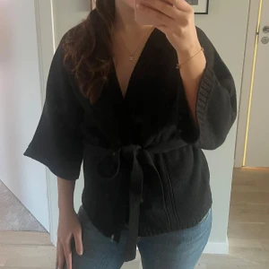 Svart omlottkofta från Vero Moda - Snygg svart omlottkofta från Vero Moda med knytband i midjan. Koftan har trekvartsärmar och en v-ringad design.