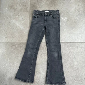 Grå bootcut jeans  - Snygga grå bootcut jeans med klassisk femficksdesign och knappgylf. Perfekta för en avslappnad stil med en touch av retro. De har en lätt tvättad look som ger dem en cool edge.