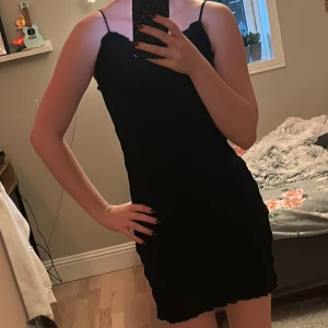 Svart klänning från H&M - Snygg svart klänning från H&M med smala axelband och en åtsittande passform. Perfekt för en stilren look. Klänningen har en ribbad struktur som ger en extra touch. Passar bra till olika tillfällen.