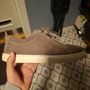Grå sneakers från Christian Louboutin - Snygga grå sneakers från Christian Louboutin med vit sula och snörning. Skorna har en stilren design och är tillverkade i mocka. Perfekta för en trendig look.
