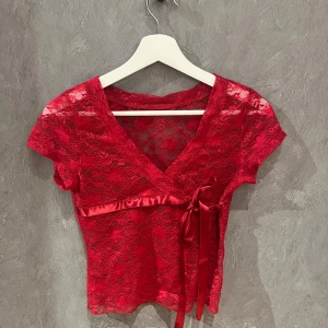 Röd spetsblus med knytband - Snygg röd spetsblus med korta ärmar och v-ringning. Tror storlek s
