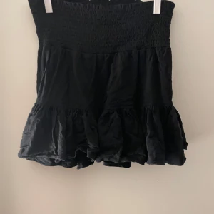 Svart kjol med volangdetaljer - Snygg svart kjol från 157 i storlek XS. Kjolen har en elastisk midja och volangdetaljer som ger en fin och lekfull look. Perfekt för att styla med olika toppar och accessoarer.