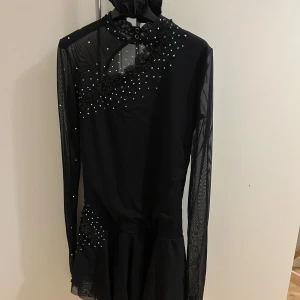 Konståkningsklänning från Sagester - Svart konståknings klänning från Sagester. Medföljer scrunchie, galge och ”väska” att bära den i. Dräkten är lite snedskuren i kjolen på sidan, där fram och bak. Storleken är XL barn och passar mig som är mellan S-M och 170 lång, kjolen är lite lång dock. Köpt från Tinas skate shop för 4000 och endast använd på 2 tävlingar därav priset. 