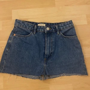 Blå kjol från Lindex - Snygga blå jeanskjol från Lindex med rå kant och klassisk femficksdesign. De har en knapp och dragkedja framtill.